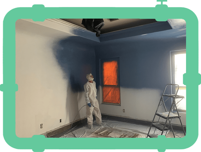 A man in white suit painting the wall of a room.