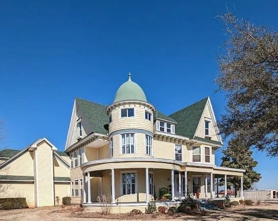 A large white house with green roof and a tree.